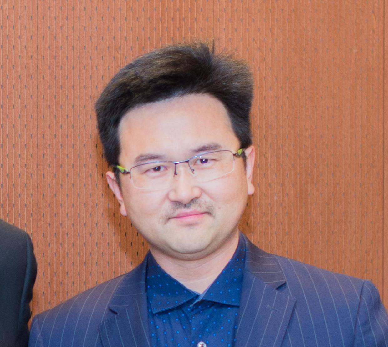 David Xiulei Ji in front of wooden backdrop