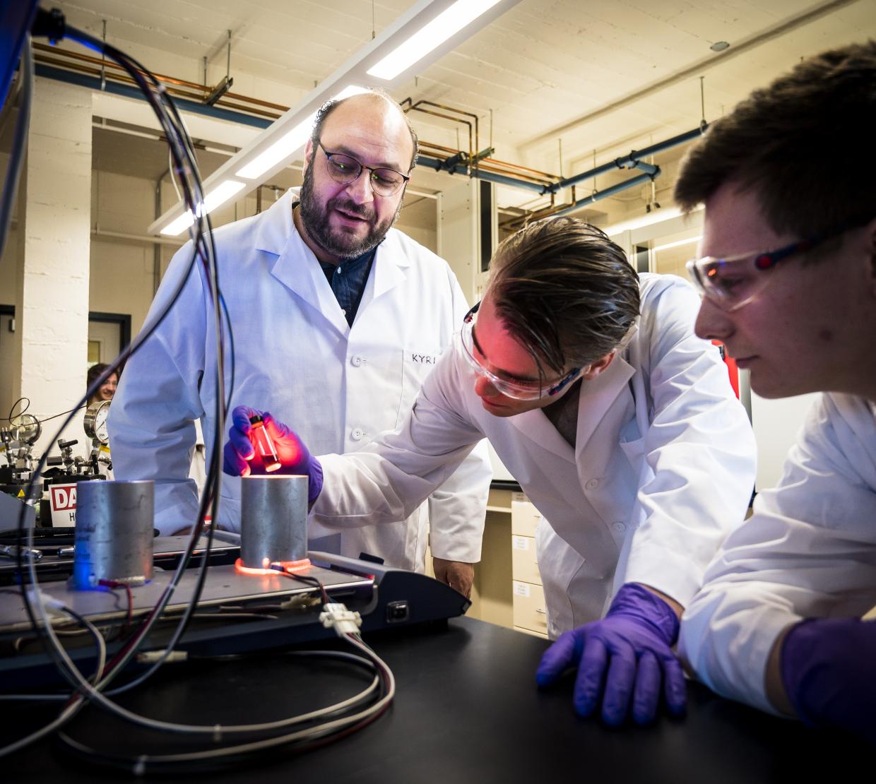 Three individuals in lab coats look at a vial. 