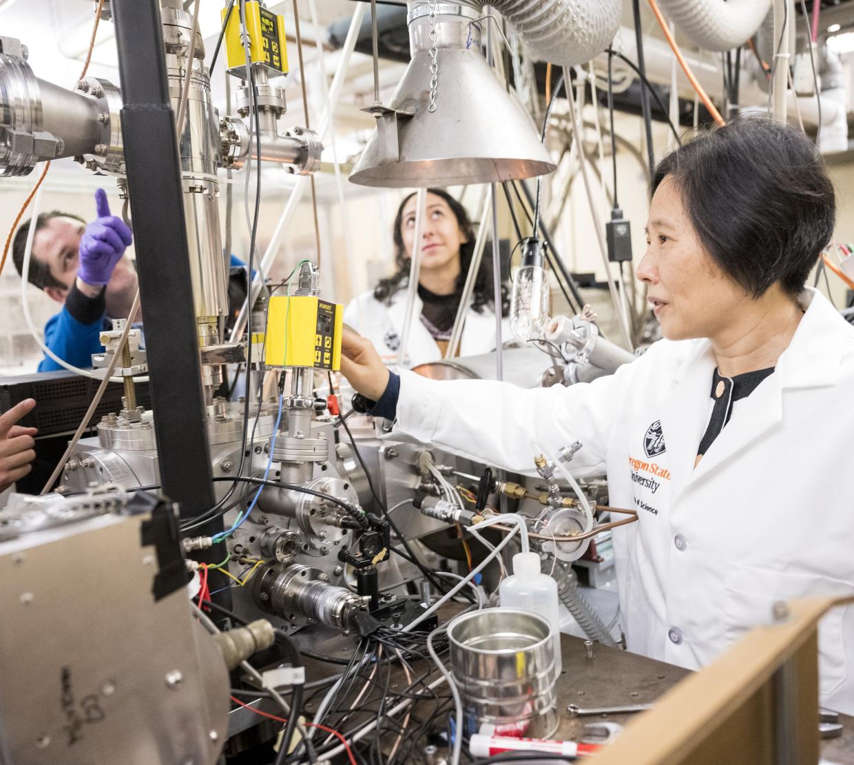 Wei Kong and graduate students work in the lab on a huge machine with wires.