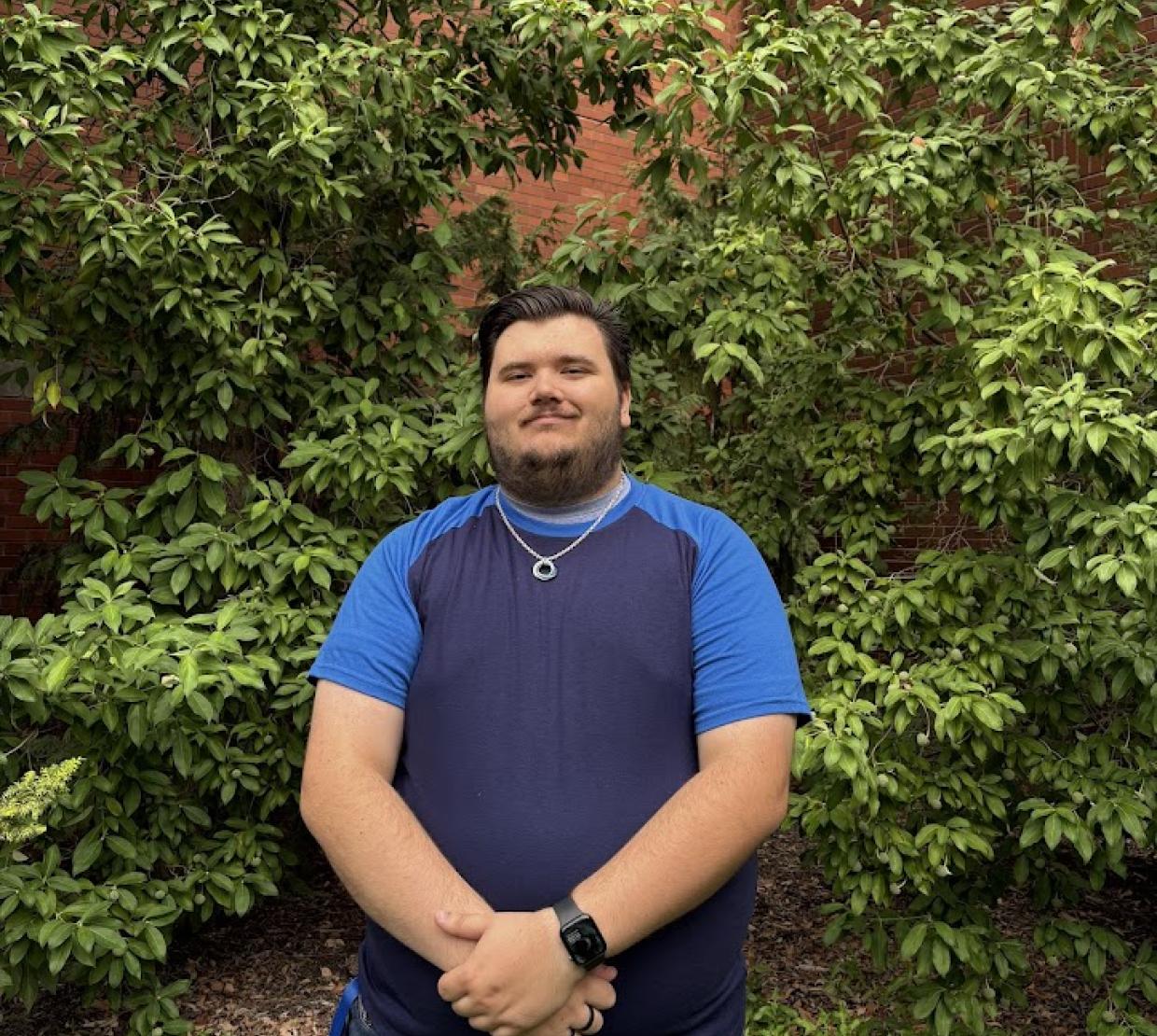 A smiling man stands outside the chemistry building with hands clasped