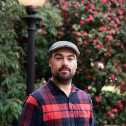 headshot of Tim Zuehlsdorff in flannel and a cap on campus in the spring