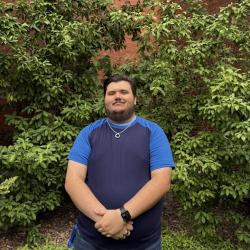A smiling man stands outside the chemistry building with hands clasped