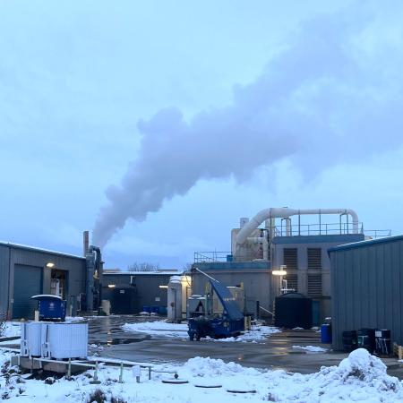 A factory building with smoke from a smokestack in a snowy winter setting with 