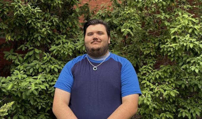 A smiling man stands outside the chemistry building with hands clasped