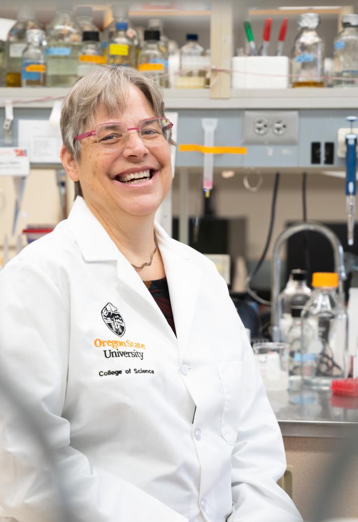 A woman in a white lab coat sits on a stool in a laboratory.