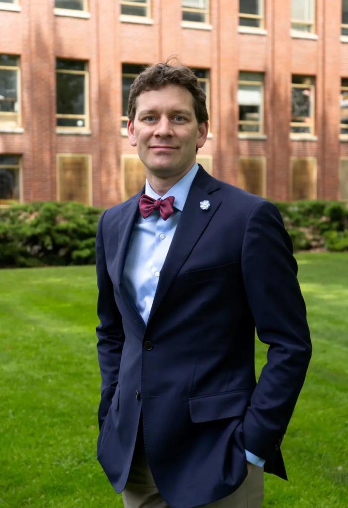 A man in a blue suit with a red bowtie poses for a photo.
