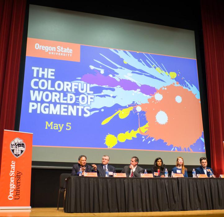 panel sitting on stage in front of event poster