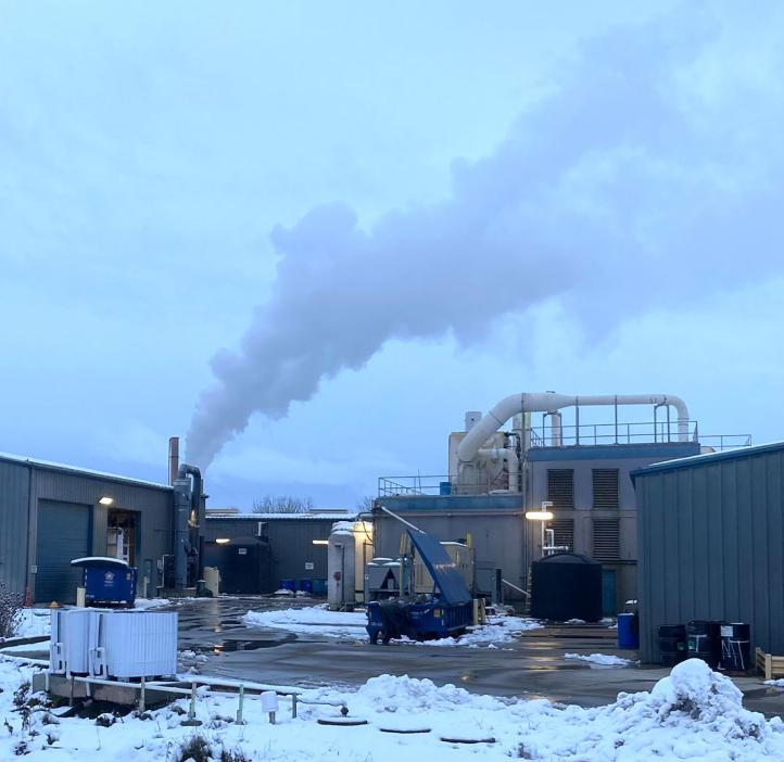 A factory building with smoke from a smokestack in a snowy winter setting with 
